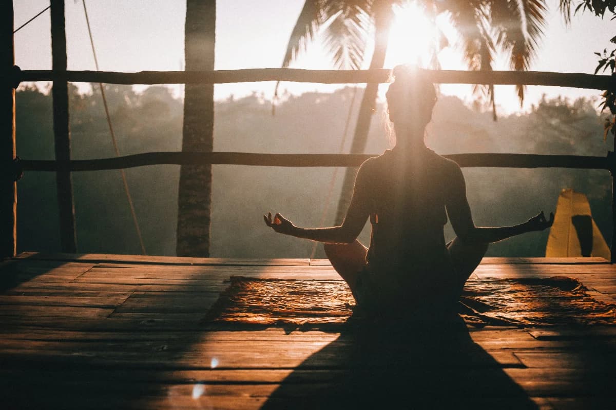 A woman sitting in meditation on a wooden deck at sunrise, facing the Costa Rican jungle